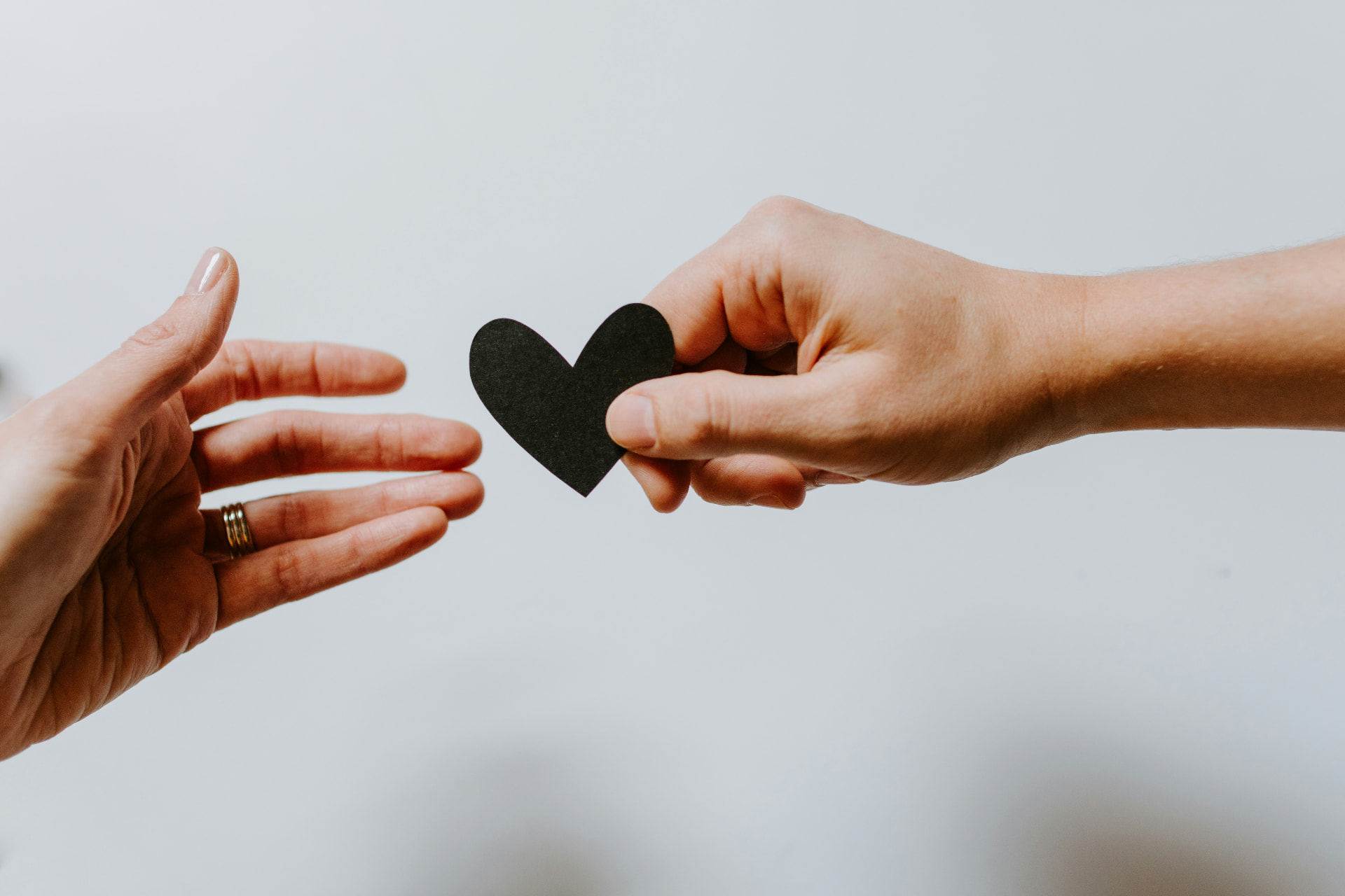 One hand gently passing a small paper heart to another open hand